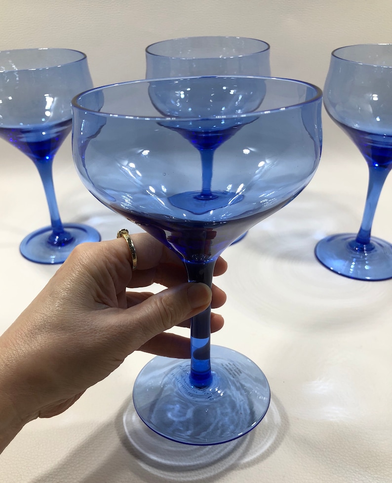May include: Set of four cobalt blue glass wine glasses with a wide bowl and a long stem. The glasses are clear and have a slight blue tint.