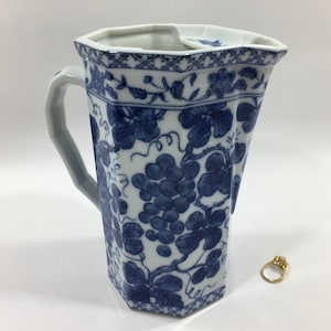 May include: A white ceramic pitcher with a blue and white grapevine design. The pitcher has a handle and a spout. It is octagonal in shape.