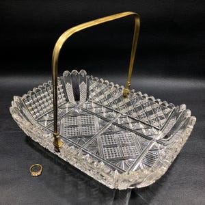 May include: A clear glass serving basket with a brass handle. The basket has a geometric pattern and is perfect for serving fruit, bread, or other snacks.