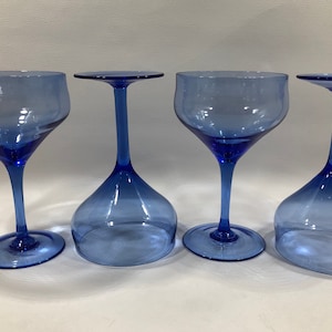 May include: Four blue glass wine glasses with a clear, slightly tinted blue colour. The glasses have a wide bowl and a long, thin stem.