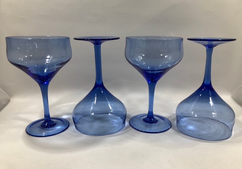 May include: Four blue glass wine glasses with a clear, slightly tinted blue colour. The glasses have a wide bowl and a long, thin stem.
