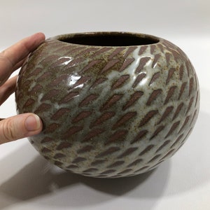 以下が含まれることがあります： 茶色と白の釉薬をかけた丸い陶器の花瓶。釉薬は斜めの線のテクスチャパターンになっています