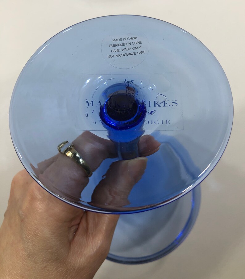May include: Blue glass goblet with a stem and a wide base. The base has a sticker that reads "Made in China, Fabriqu&eacute; en Chine, Hand Wash Only, Not Microwave Safe" and "Mark &  Spikes, Anthropologie".