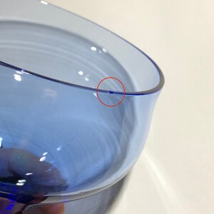 May include: Close-up of a blue glass vase with a small chip on the rim.