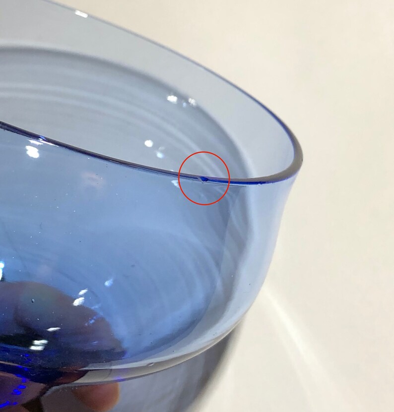May include: Close-up of a blue glass vase with a small chip on the rim.