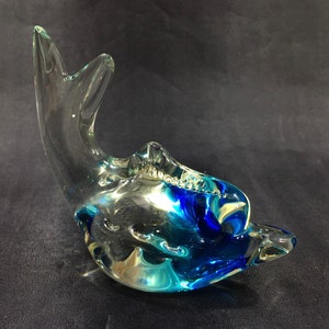 May include: A glass dolphin figurine with blue and green swirls. The dolphin is made of clear glass with a blue and green swirl design.