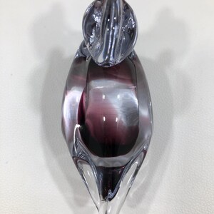 May include: A clear glass sculpture with a purple and white swirl design. The art glass piece has a rounded top and a pointed base. The sculpture is a decorative object.