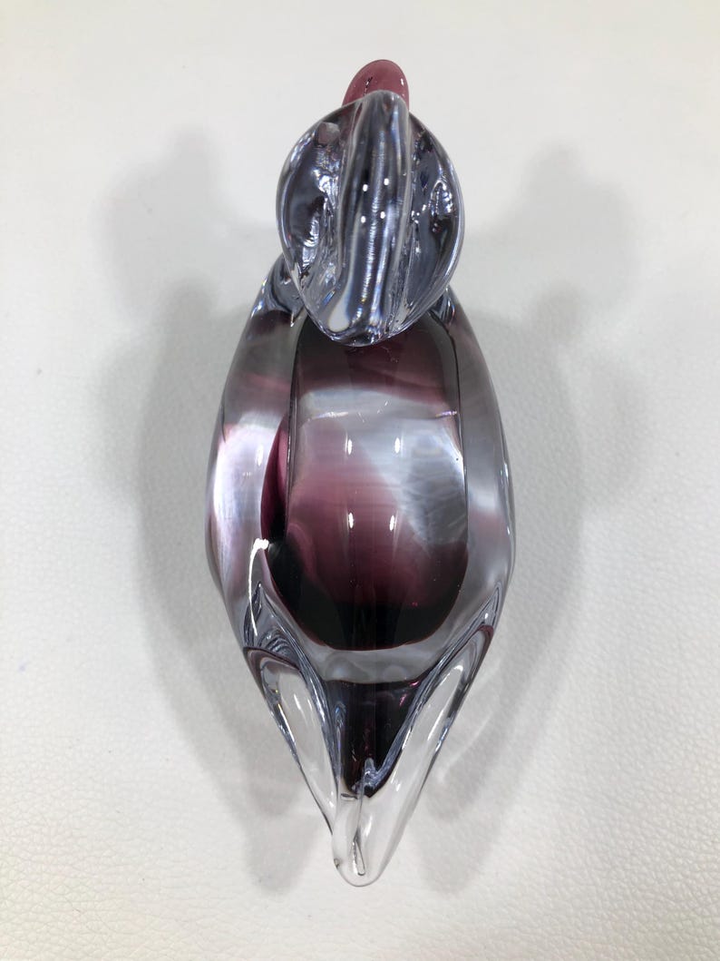 May include: A clear glass sculpture with a purple and white swirl design. The art glass piece has a rounded top and a pointed base. The sculpture is a decorative object.