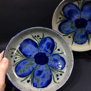 May include: Two ceramic plates with a blue and green floral design. The plates have a speckled glaze and a white background.