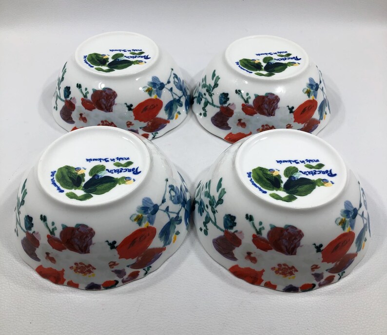 May include: Four white porcelain bowls with a floral design. The bowls feature a pattern of red, blue, and green flowers and foliage. The bottom of each bowl has a green and blue floral design and the text "Porcelain made in Sweden".