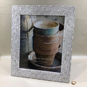 May include: A white rectangular picture frame with a floral lace design. The frame holds a photograph of stacked terracotta pots and a small bowl. The frame is labeled "valerie bertinelli" and is 8" x 10".