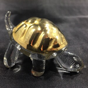 May include: A glass turtle figurine with a gold-painted shell. The turtle is walking forward with its head raised.