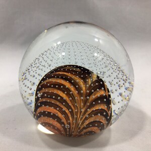 May include: A clear glass paperweight with a swirling brown and gold design inside. The paperweight is filled with small air bubbles.