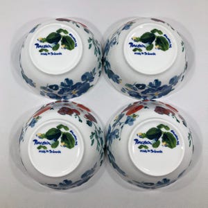May include: Four white porcelain bowls with floral designs in blue, red, and green. The bowls have a rounded shape and are decorated with flowers and leaves. The text "Porcelain made in Indonesia" is printed on the bottom of each bowl.