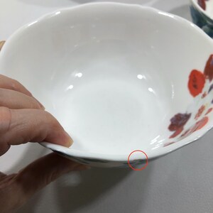 May include: White ceramic bowl with a scalloped rim and floral design in red, orange, and purple. The bowl has a smooth, glossy finish and a simple, elegant design, suitable for serving food.
