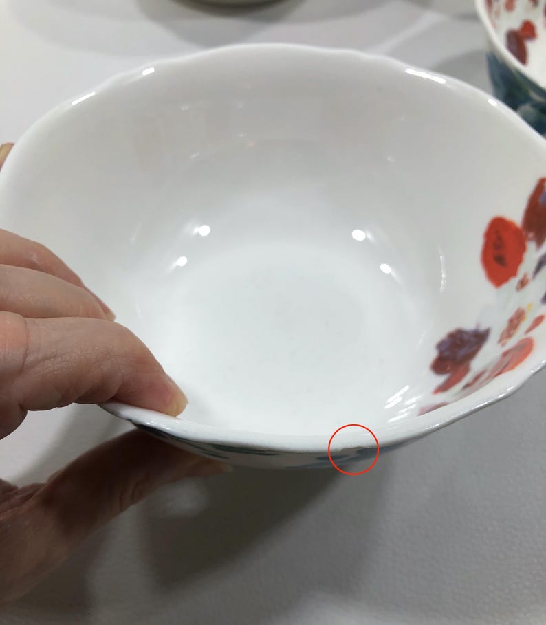 May include: White ceramic bowl with a scalloped rim and floral design in red, orange, and purple. The bowl has a smooth, glossy finish and a simple, elegant design, suitable for serving food.