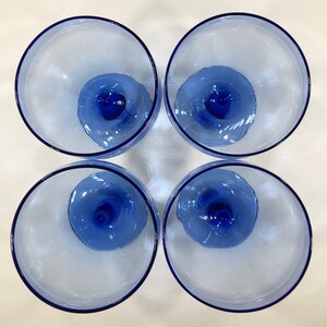 May include: Four blue glass wine glasses with a clear base and a blue rim. The glasses are arranged in a square pattern.
