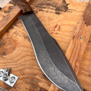 heavy duty chopper blade with stonewashed finish photographed next to stitched leather sheath