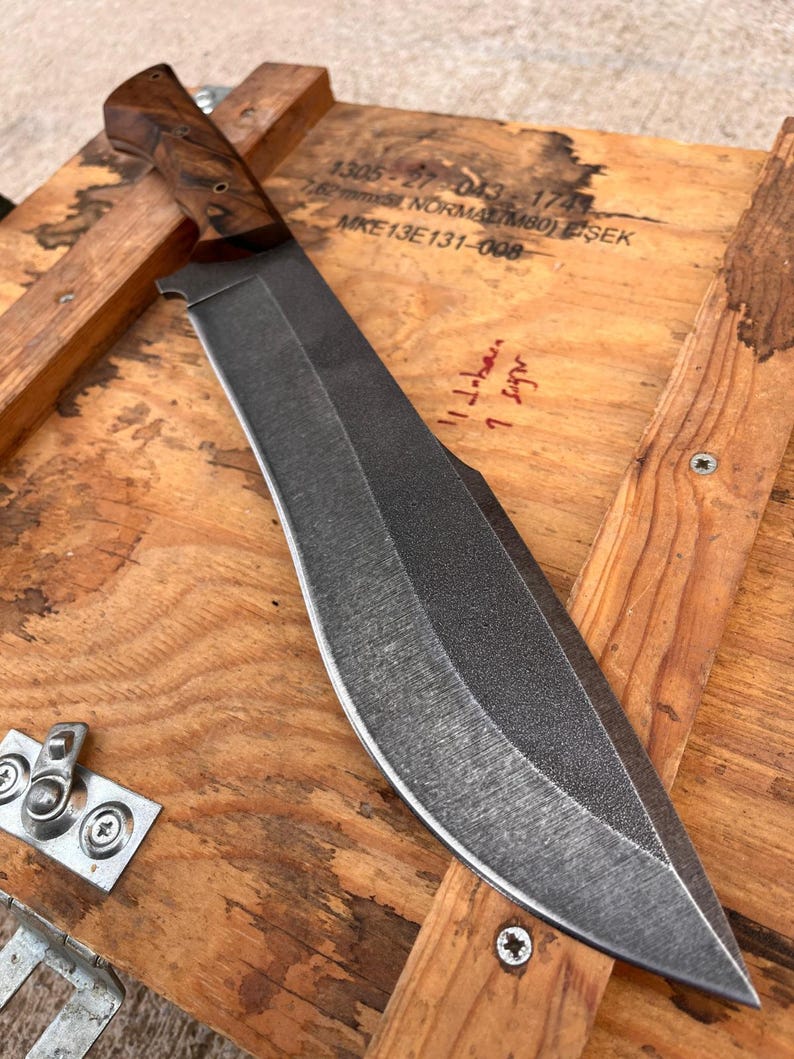 heavy duty chopper blade with stonewashed finish photographed next to stitched leather sheath