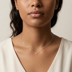 May include: A fine silver necklace with a small, round, clear gemstone pendant. The necklace is worn around the neck, highlighting the minimalist design and subtle elegance of the jewellery. The pendant is the focal point.