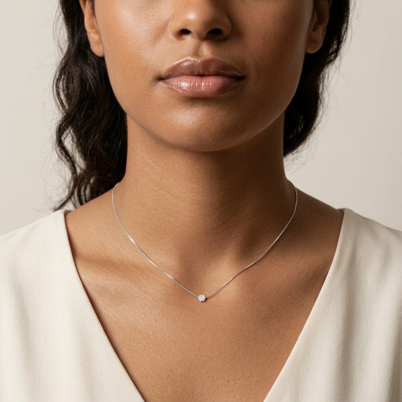 May include: A fine silver necklace with a small, round, clear gemstone pendant. The necklace is worn around the neck, highlighting the minimalist design and subtle elegance of the jewellery. The pendant is the focal point.
