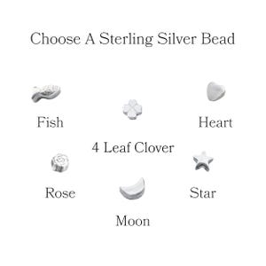 May include: Image showing a selection of sterling silver beads. The beads include a fish, a four-leaf clover, a heart, a rose, a moon, and a star. Text at the top reads "Choose A Sterling Silver Bead", with labels under each bead.