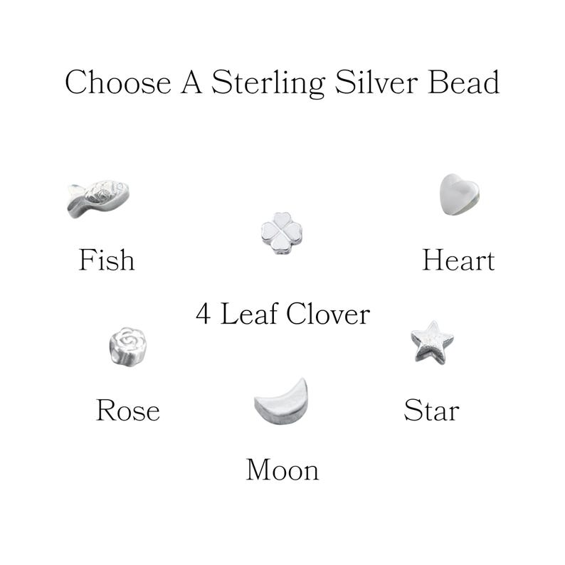 May include: Image showing a selection of sterling silver beads. The beads include a fish, a four-leaf clover, a heart, a rose, a moon, and a star. Text at the top reads "Choose A Sterling Silver Bead", with labels under each bead.