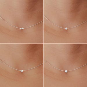 May include: Four necklaces featuring tiny silver pendants: a fish, a flower, a heart, and a four-leaf clover. Each pendant hangs from a fine, transparent chain, giving a floating illusion. The pendants are small and silver-coloured.