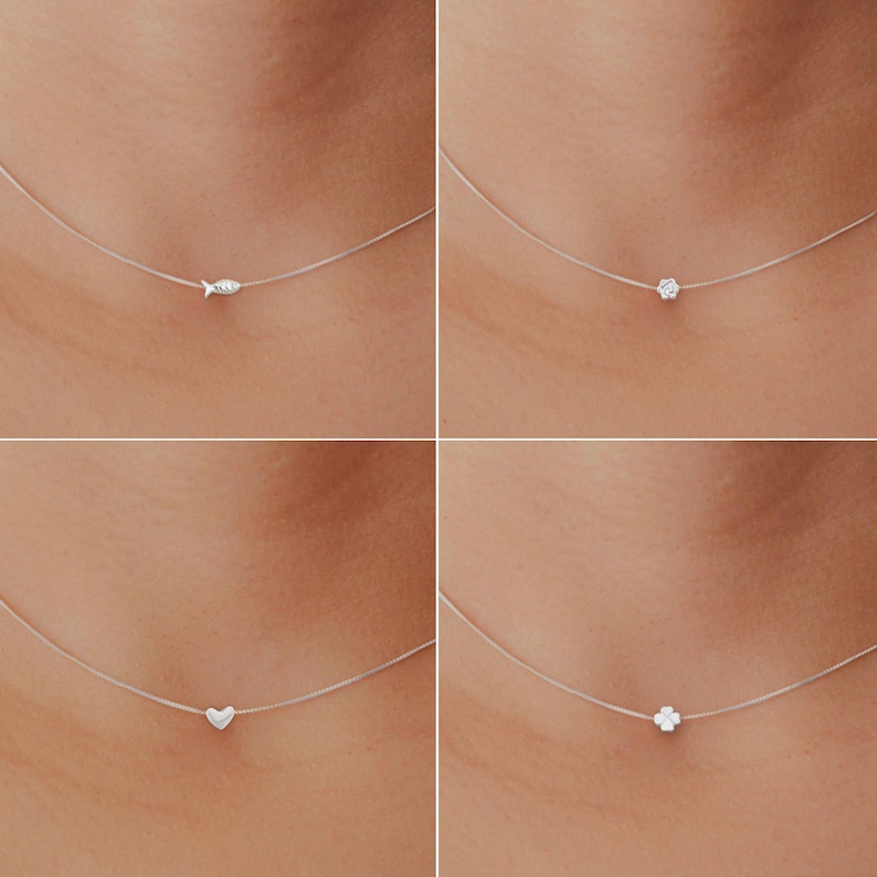 May include: Four necklaces featuring tiny silver pendants: a fish, a flower, a heart, and a four-leaf clover. Each pendant hangs from a fine, transparent chain, giving a floating illusion. The pendants are small and silver-coloured.