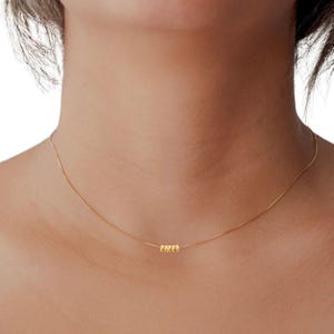 May include: A delicate gold necklace featuring a thin chain and a cluster of five small, round beads. The necklace is worn around the neck, showcasing its minimalist design and subtle elegance. The gold color provides a warm, classic look.