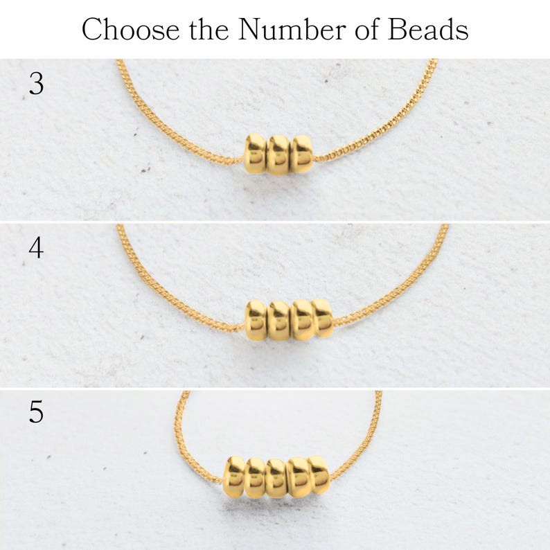 May include: Gold-colored necklaces with varying numbers of beads: three, four, and five. The text "Choose the Number of Beads" is at the top. The necklaces are displayed on a light-colored surface.