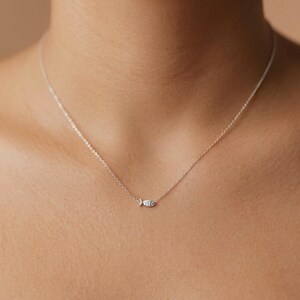 May include: A delicate silver necklace featuring a small fish pendant. The pendant has a detailed design, and the chain is thin and elegant. The necklace is shown against a neutral background, highlighting its simple beauty.