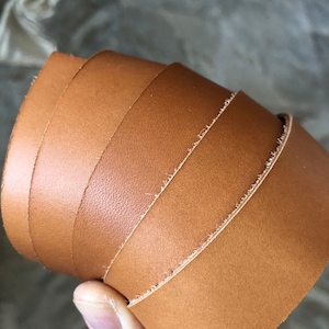 May include: Close-up of a roll of brown leather with a slightly rough texture. The leather is folded over itself several times, showing the edges of the material.