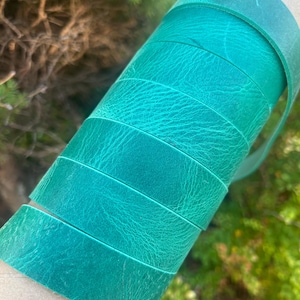 May include: A roll of teal leather strips. The leather has a textured surface and is wrapped around a cardboard tube. The colour transitions from a darker teal to a lighter shade.