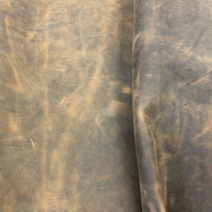 May include: A close-up of a piece of brown leather with a distressed, vintage look. The leather has a natural, uneven texture and a faded, worn appearance.