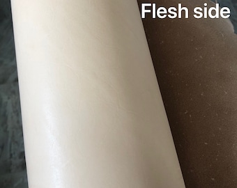 May include: A close-up of a piece of leather showing the grain side and the flesh side. The grain side is a light cream color and the flesh side is a light brown color.