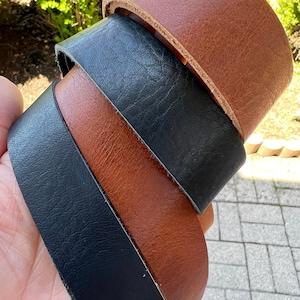 May include: Close-up of three leather strips in shades of brown and black. The top strip is a light brown, the middle is black, and the bottom is a darker brown. The leather appears to be textured and has a natural grain.