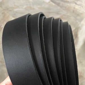 May include: A stack of black leather straps of varying widths. The straps are rolled up and have a smooth, polished finish.