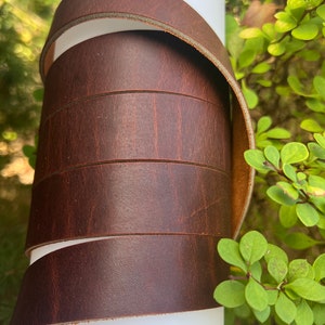 Peut inclure: Un gros plan d'une lanière en cuir marron enroulée sur une surface blanche. Le cuir a une finition naturelle et texturée.