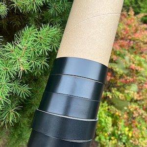 May include: Four black leather straps rolled up on a brown cardboard tube. The straps are all the same width and are stacked on top of each other.