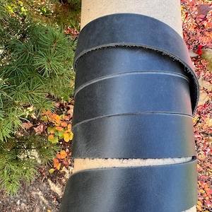 May include: A roll of black leather strap, coiled around a cardboard tube. The leather is smooth and appears to be high quality.