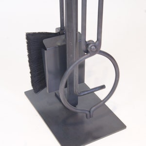May include: A black metal fireplace tool set with a brush, poker, and tongs. The tools are attached to a black metal stand.