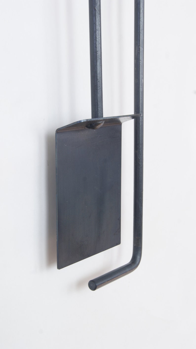 May include: A black metal fireplace tool set with a shovel, poker, and tongs. The tools are hanging on a wall mount.