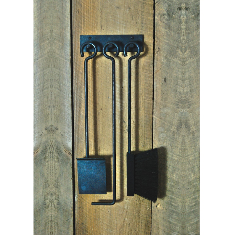 May include: Black metal fireplace tool set with a shovel, poker, and brush hanging on a wooden wall.