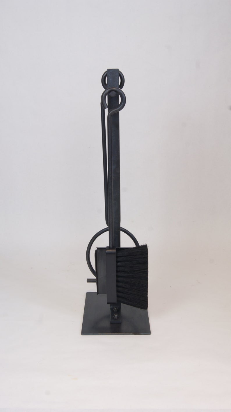 May include: Black metal fireplace tool set with a brush, poker, and shovel. The tools are attached to a stand with a black metal base.