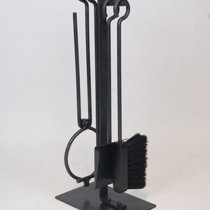 May include: Black metal fireplace tool set with a stand. The set includes a poker, tongs, brush, and shovel.