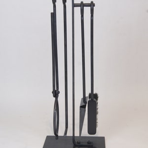 May include: A black metal fireplace tool set with a stand. The set includes a poker, shovel, tongs, and a brush.