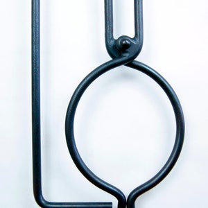 May include: A black metal tool with a circular handle and a long, straight arm. The tool is designed for holding and manipulating hot objects.