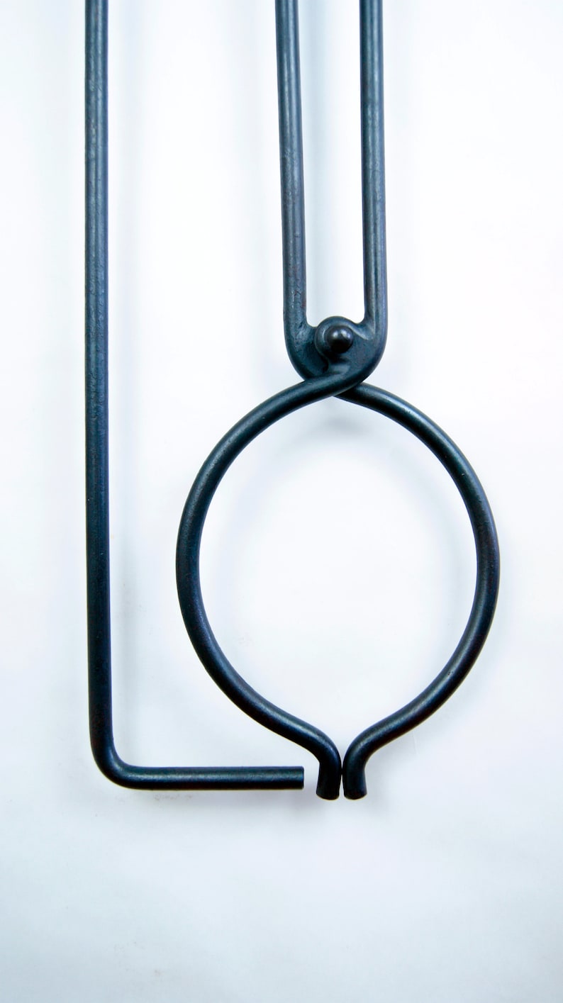 May include: A black metal tool with a circular handle and a long, straight arm. The tool is designed for holding and manipulating hot objects.