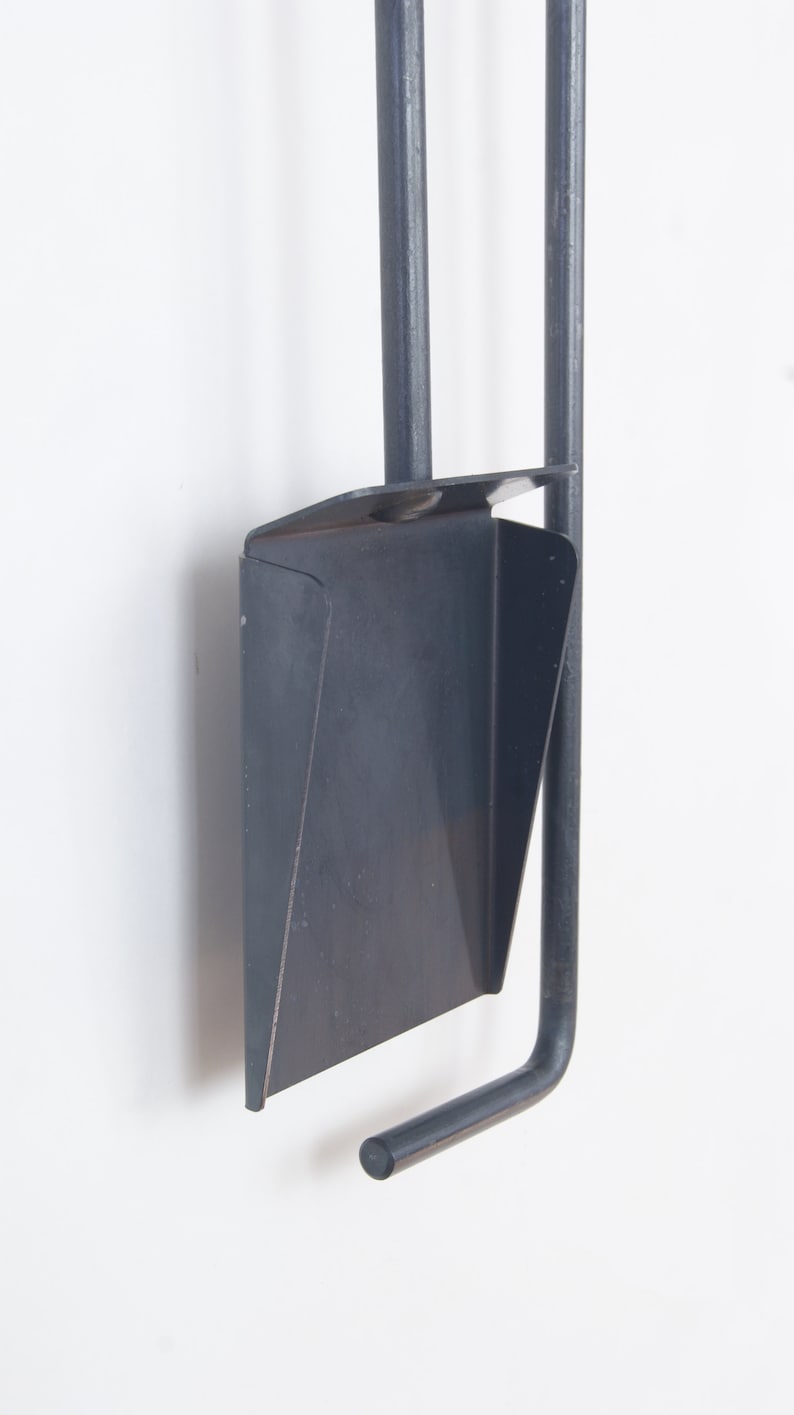 May include: A black metal fireplace tool set with a shovel, poker, and tongs. The tools are hanging on a wall.